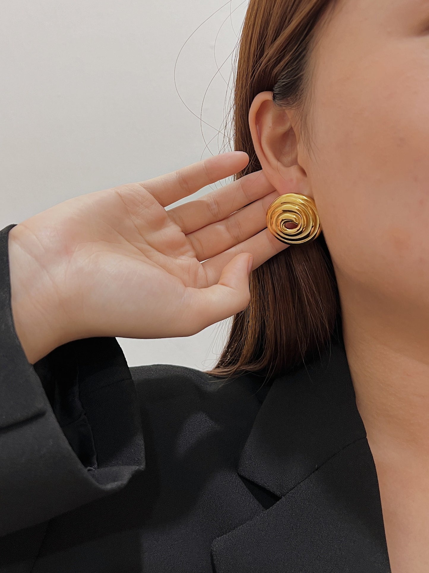 A woman wearing a vintage inspired gold circle spiral earrings pair with a black blazer