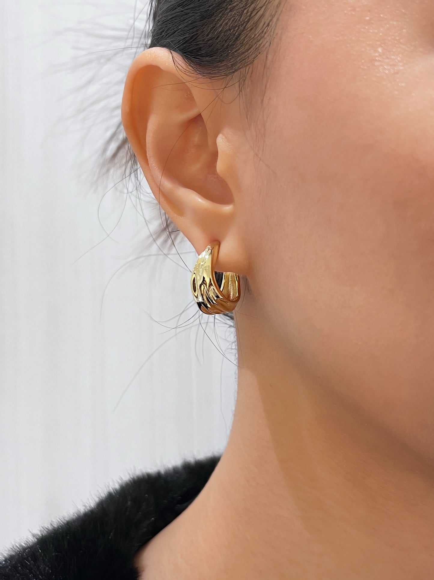 Gold hoop earring worn by a person with a blurred background