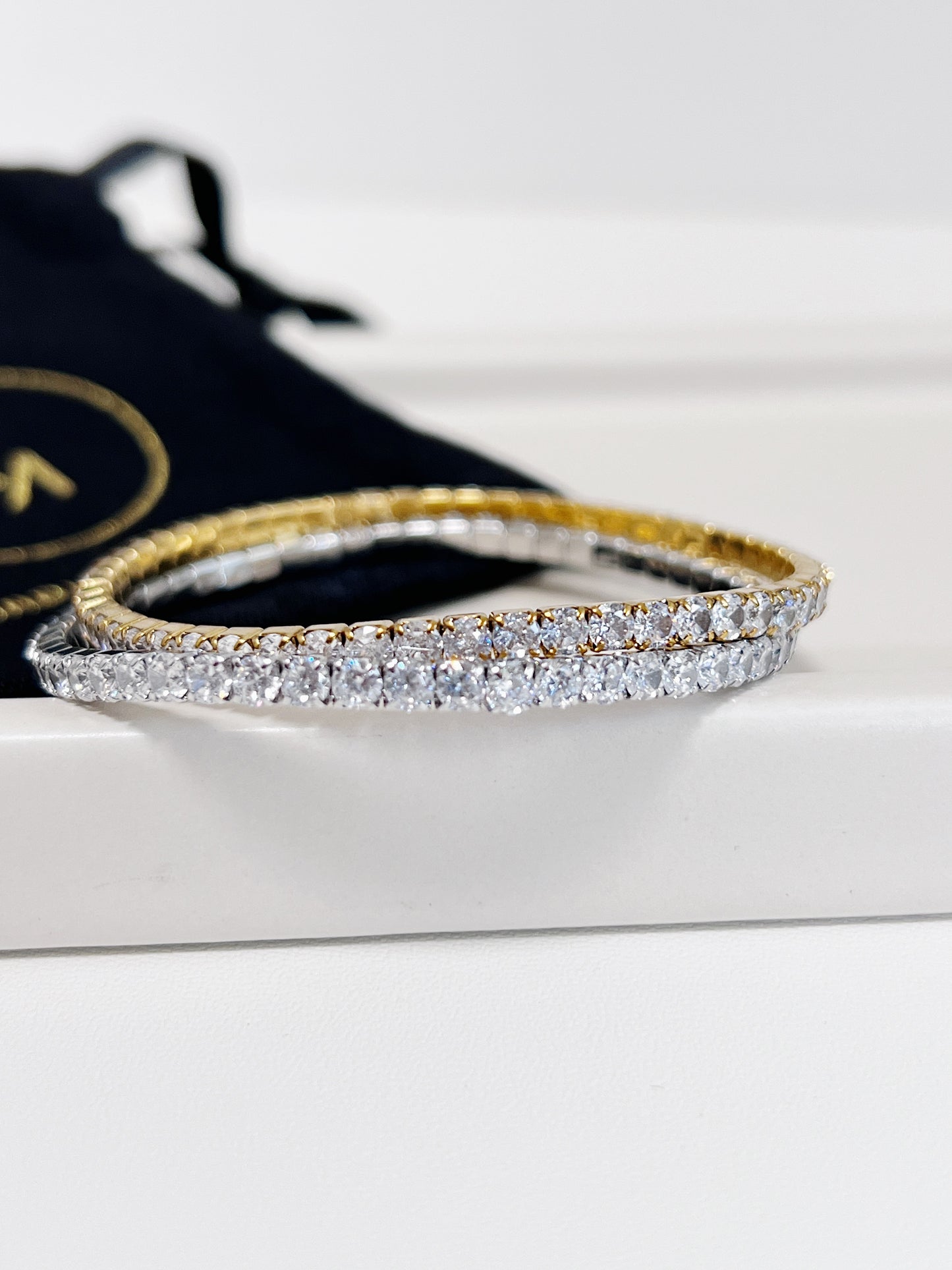 Gold and silver tennis bracelet on a white surface with a black pouch in the background