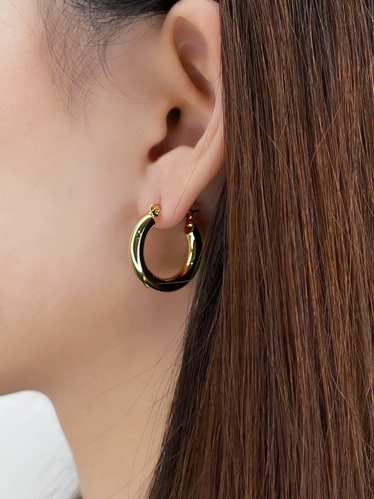 Gold hoop earring worn by a person with long brown hair.