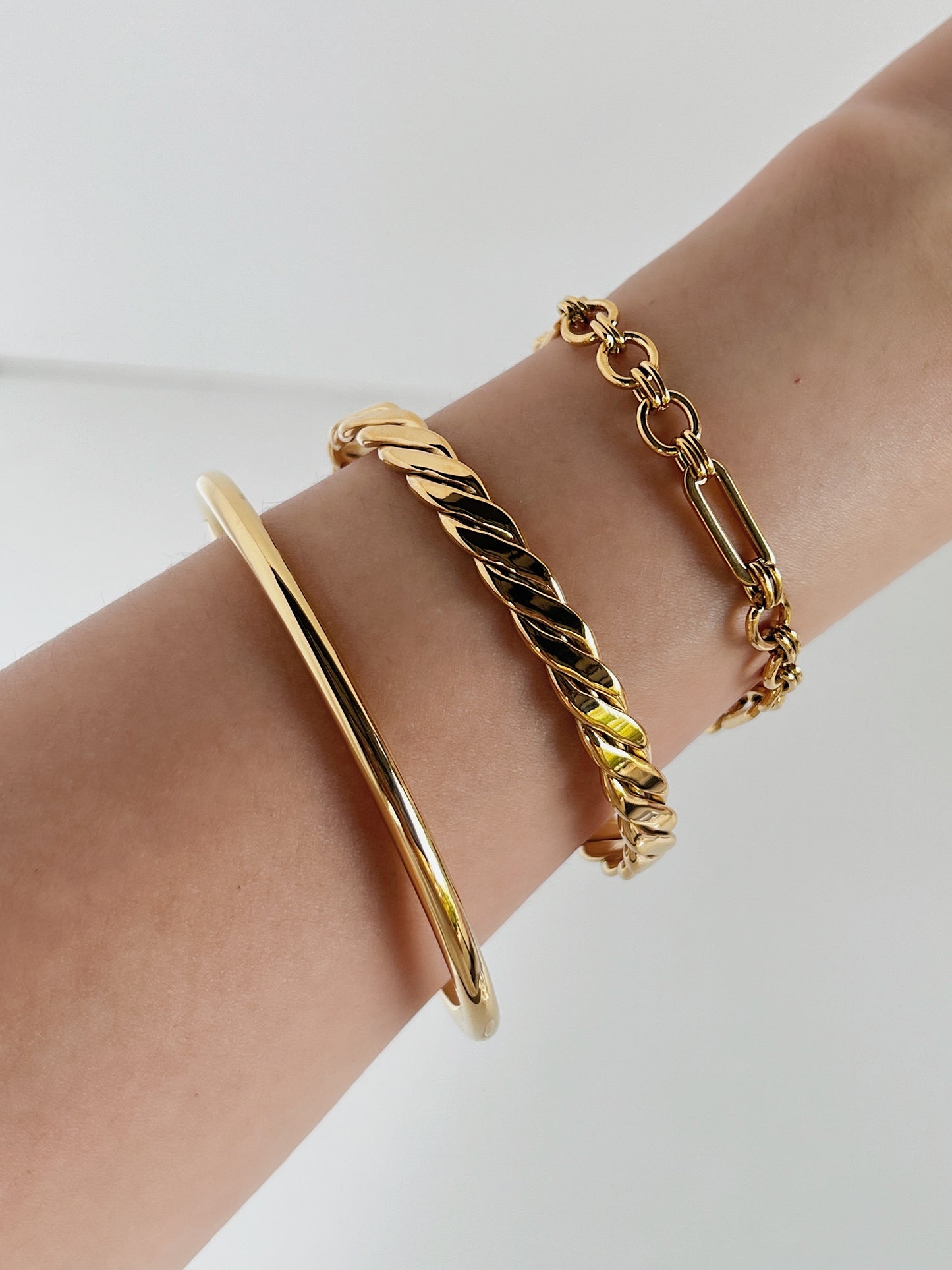 Gold stacking bracelets on a wrist against a white background