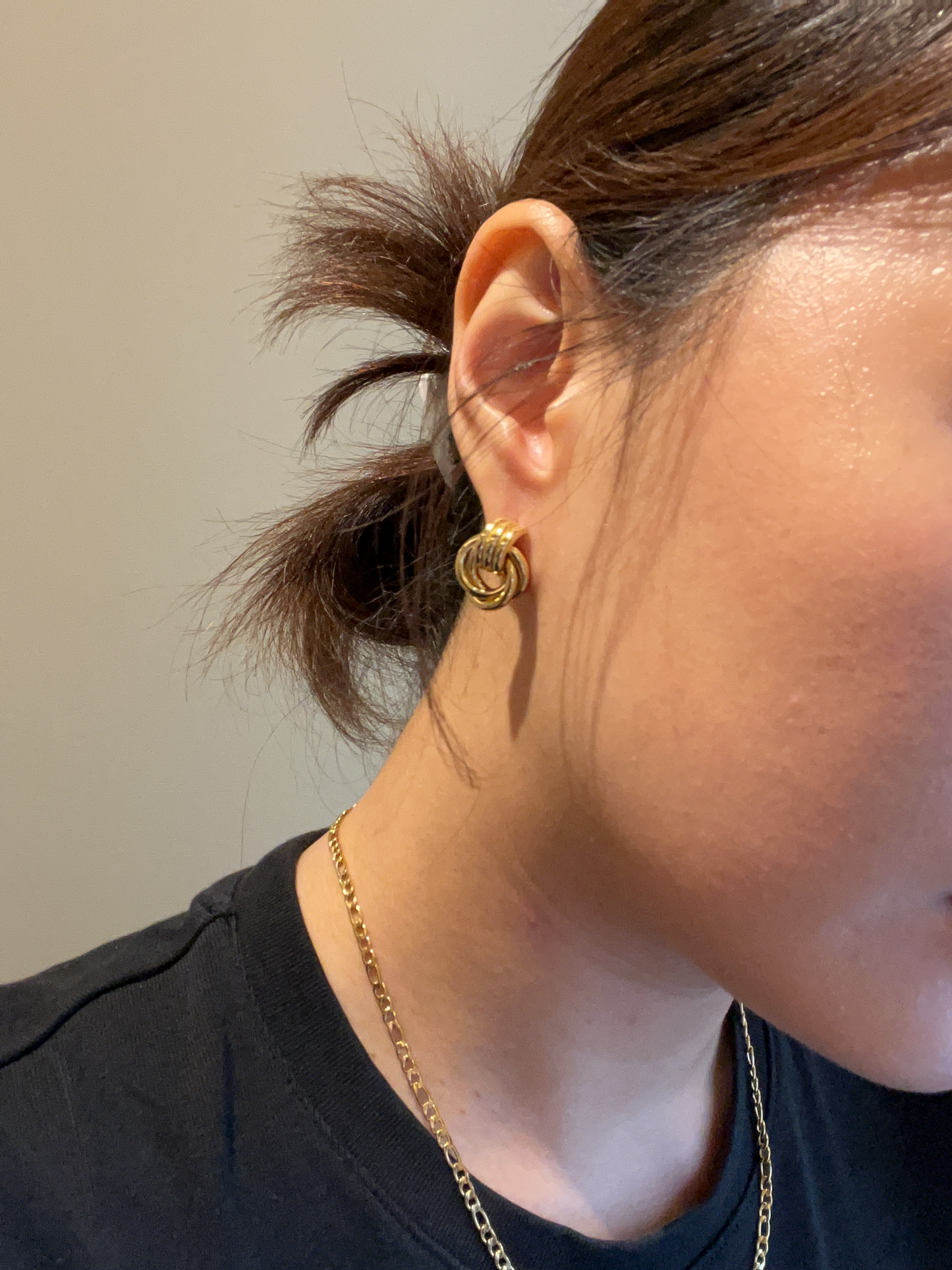 Close-up of a person wearing a gold earring and necklace against a neutral background
