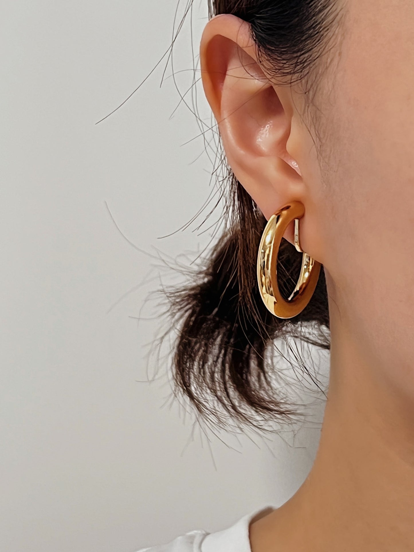 Gold hoop earrings worn by a person with a neutral background