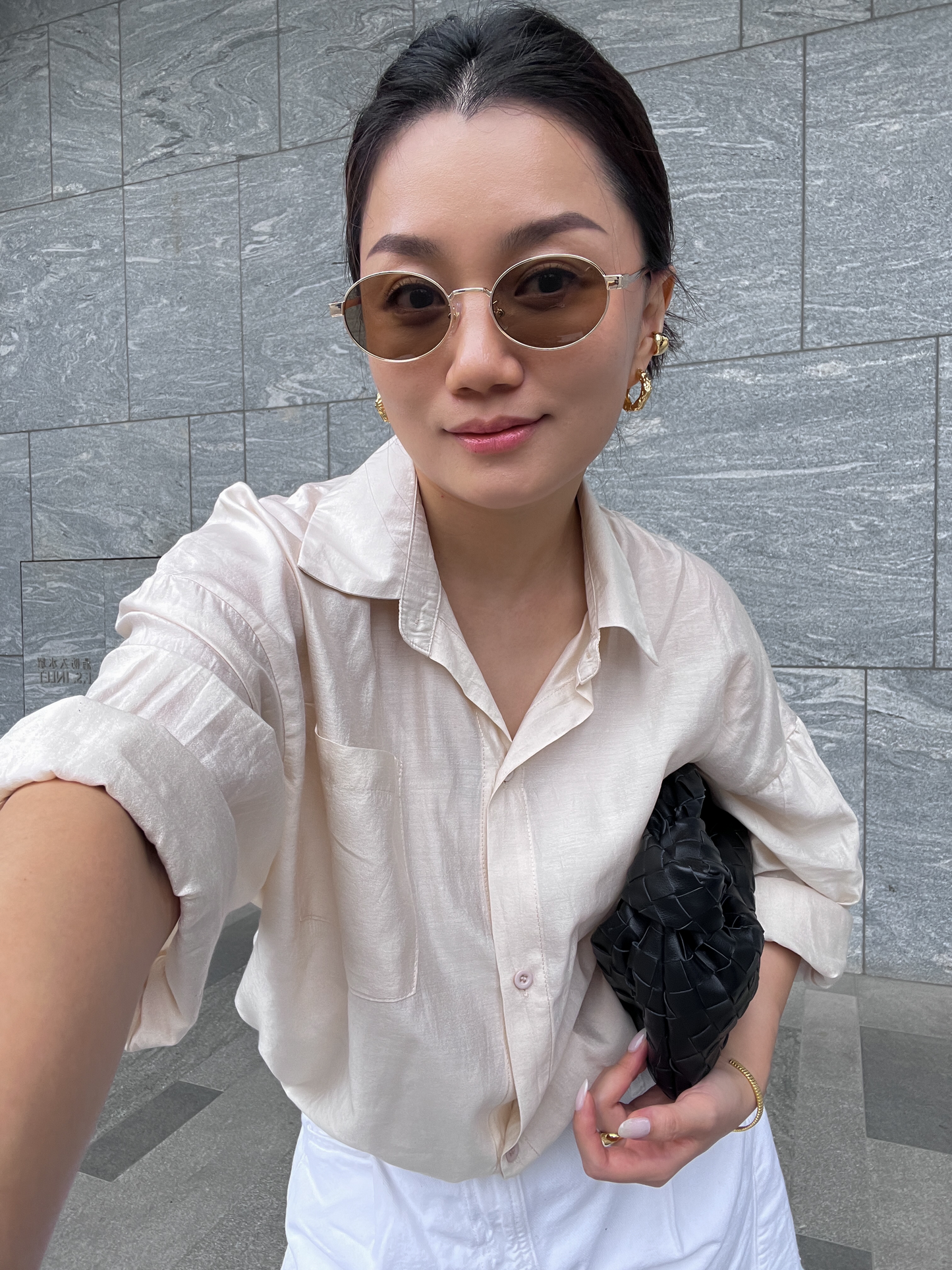 Person wearing a light-colored shirt against a gray tiled wall.
