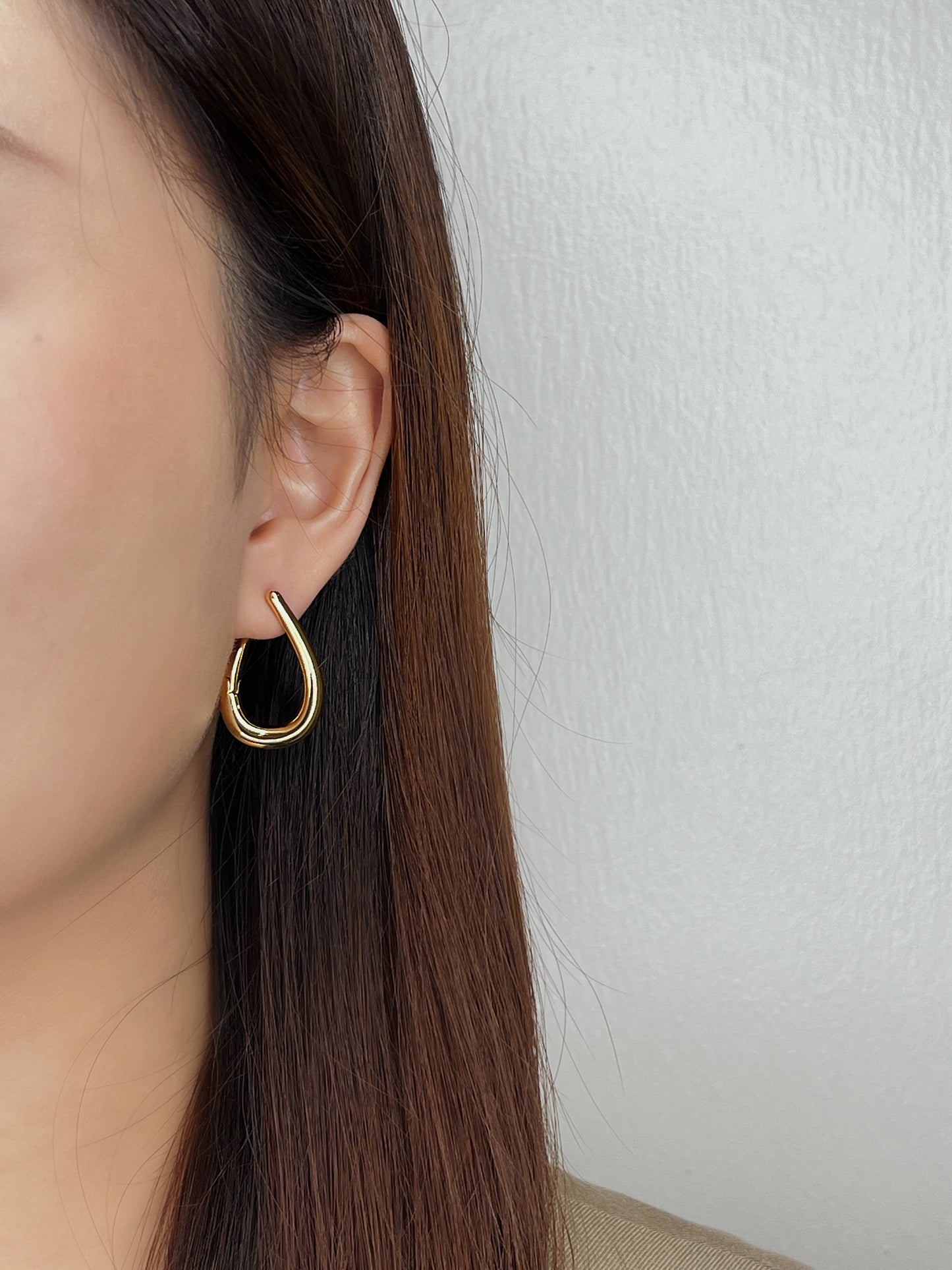 Minimalist Gold hoop earring worn by a person with long brown hair against a white background