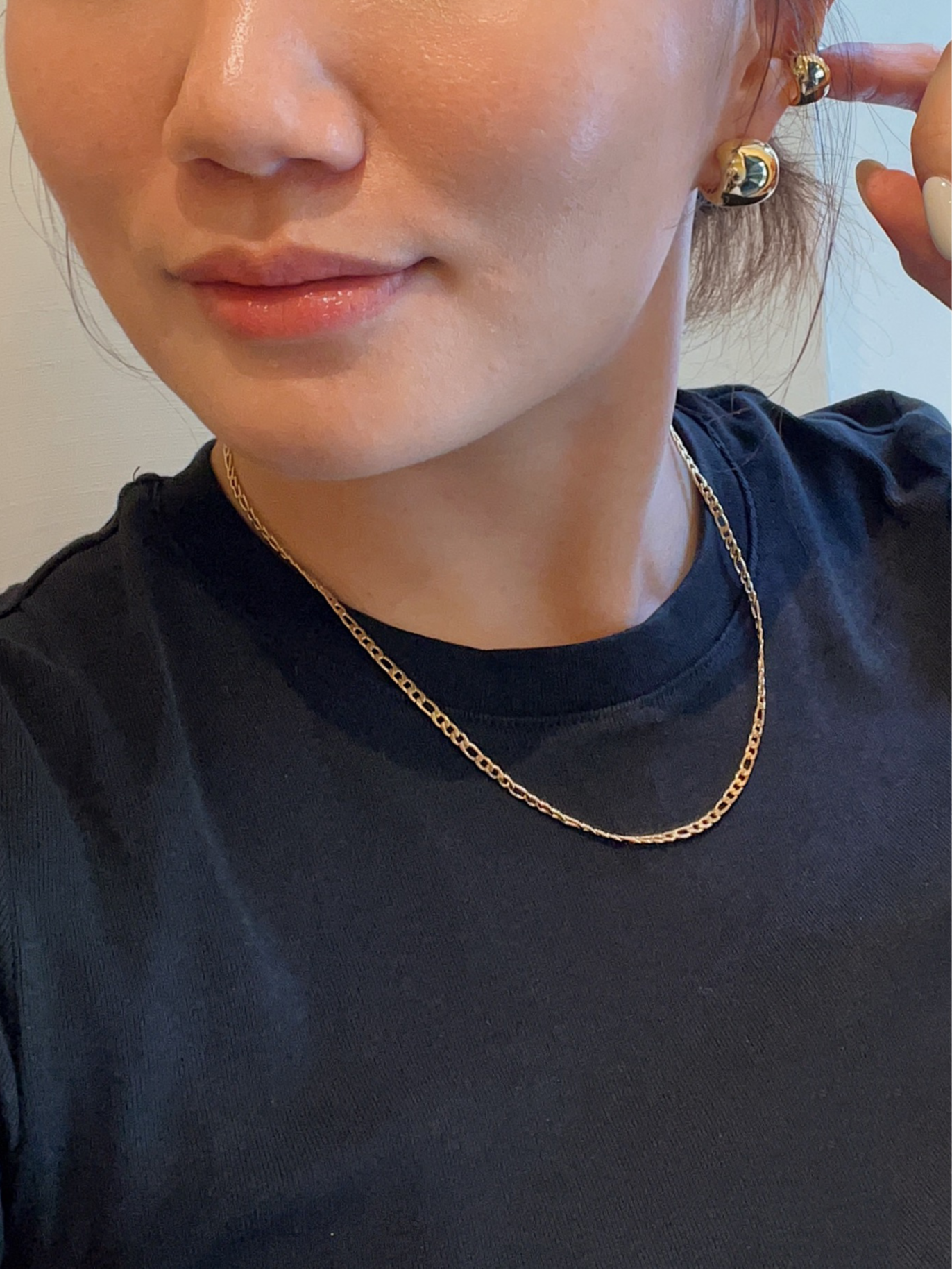 Woman wearing a gold earring and chain necklace, smiling indoors with a window in the background