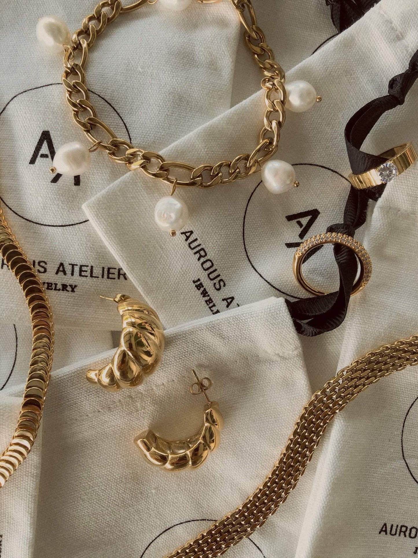 A high-end flat lay showcasing the gold Danielle mesh chain bracelet alongside textured jewelry pouches, fine rings, and pearl links at Aurous Atelier.