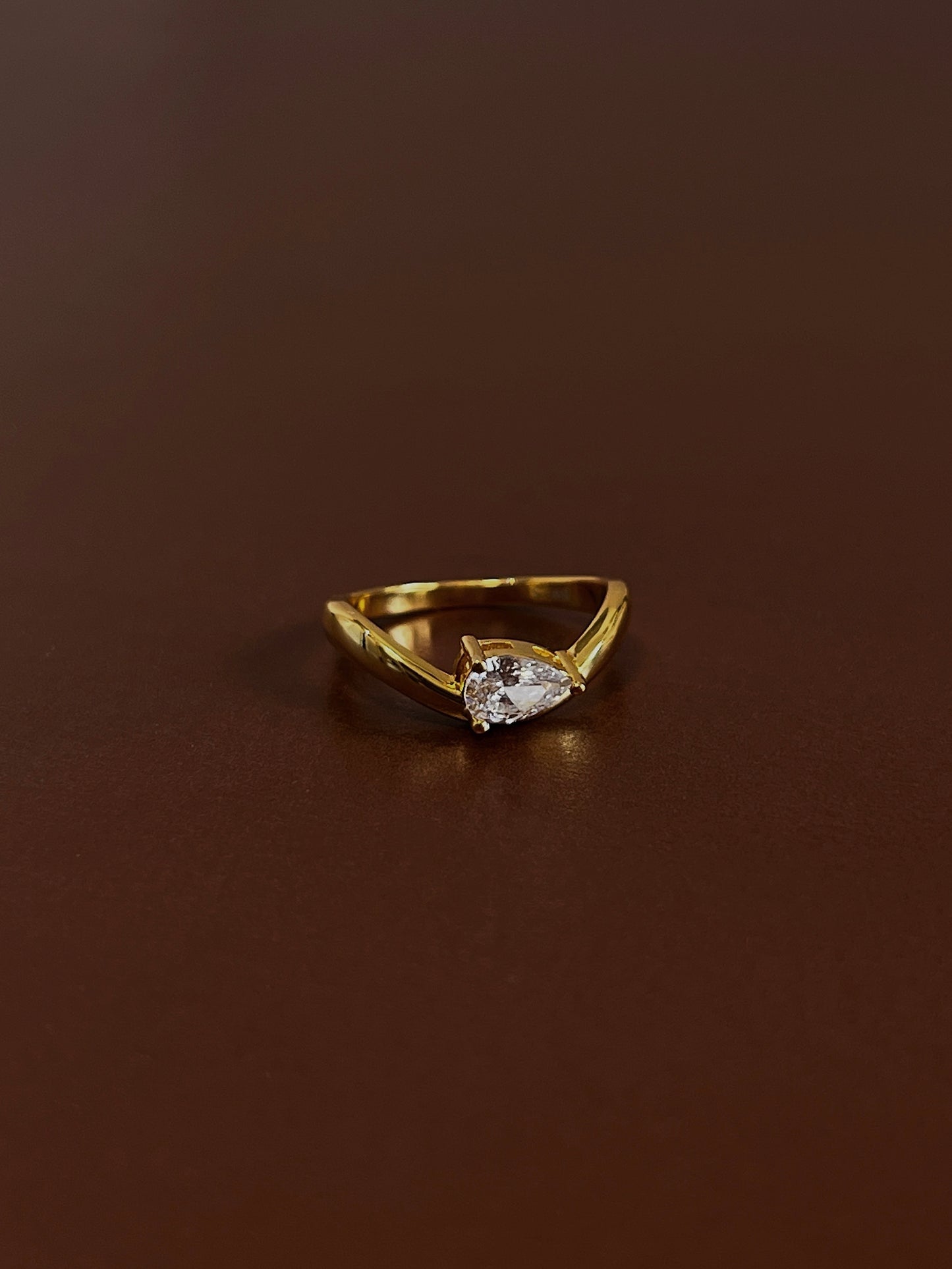 Nova pear solitaire wave ring in 18k gold vermeil with pear-cut moissanite stone on dark brown textured background