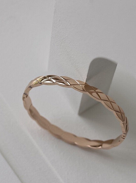 An angled close-up shot of the Corin quilted hinged bangle in a warm rose gold finish, highlighting the multi-dimensional diamond lattice texture against a minimalist geometric backdrop.
