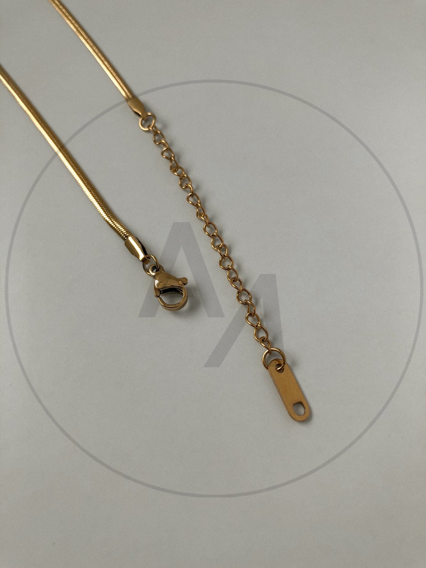 Lola herringbone gold necklace folded in circle on grey surface showing lobster clasp and extender chain