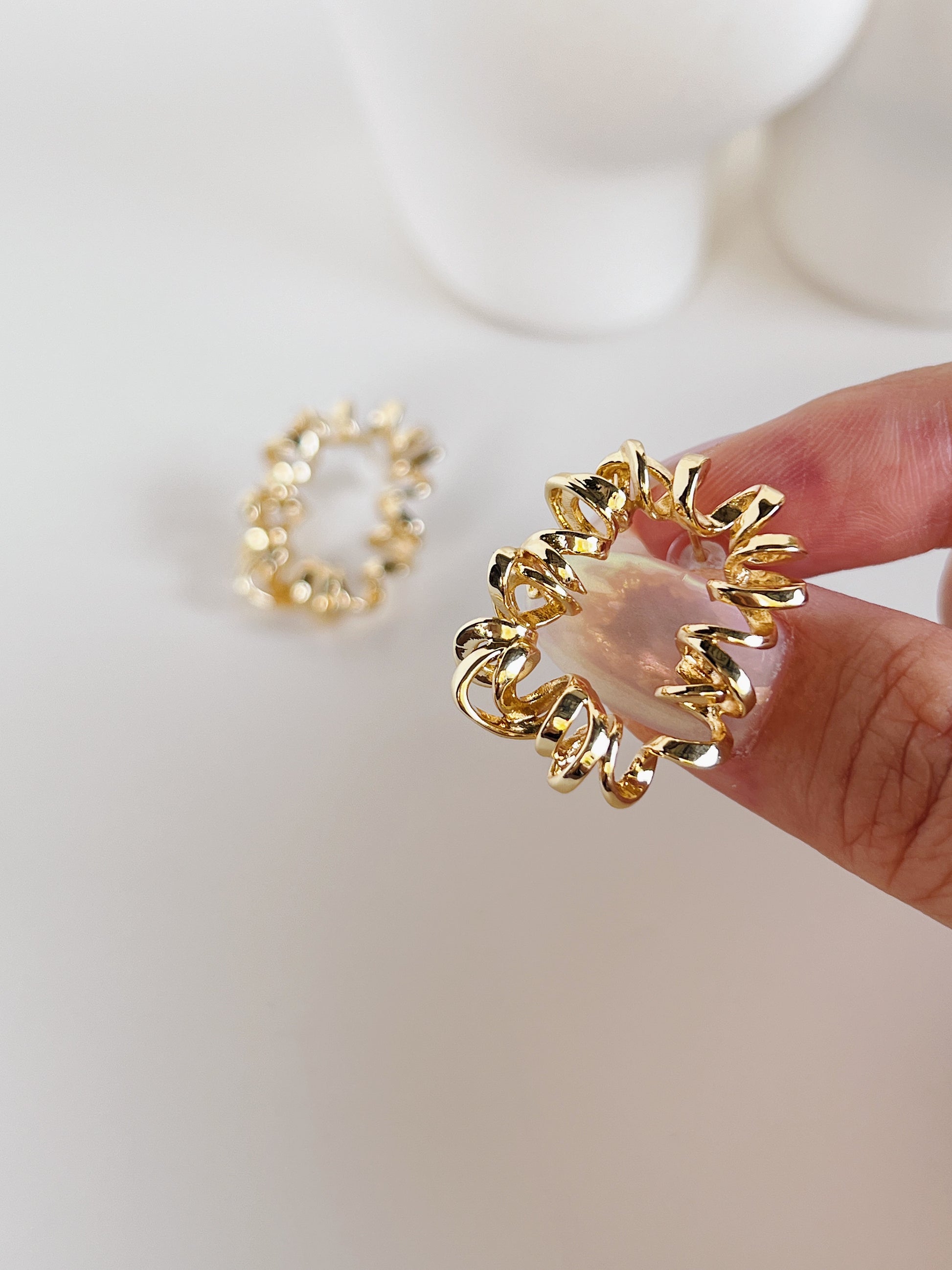 Gold earring with a textured design held by a hand on a white background