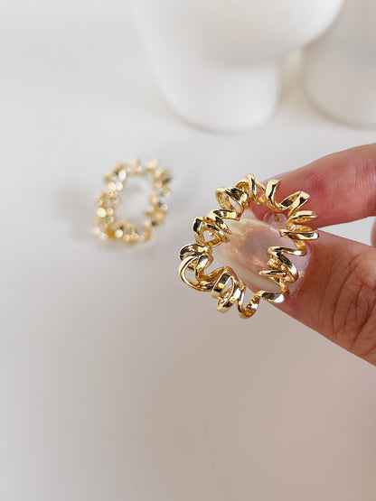 Gold earring with a textured design held by a hand on a white background