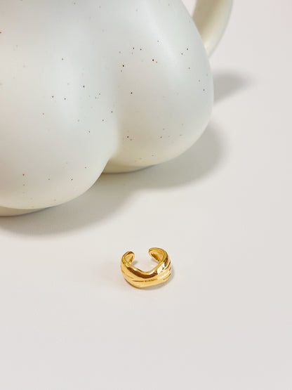 Gold crescent moon ear cuff earring on a white surface with speckled ceramic bowls in the background