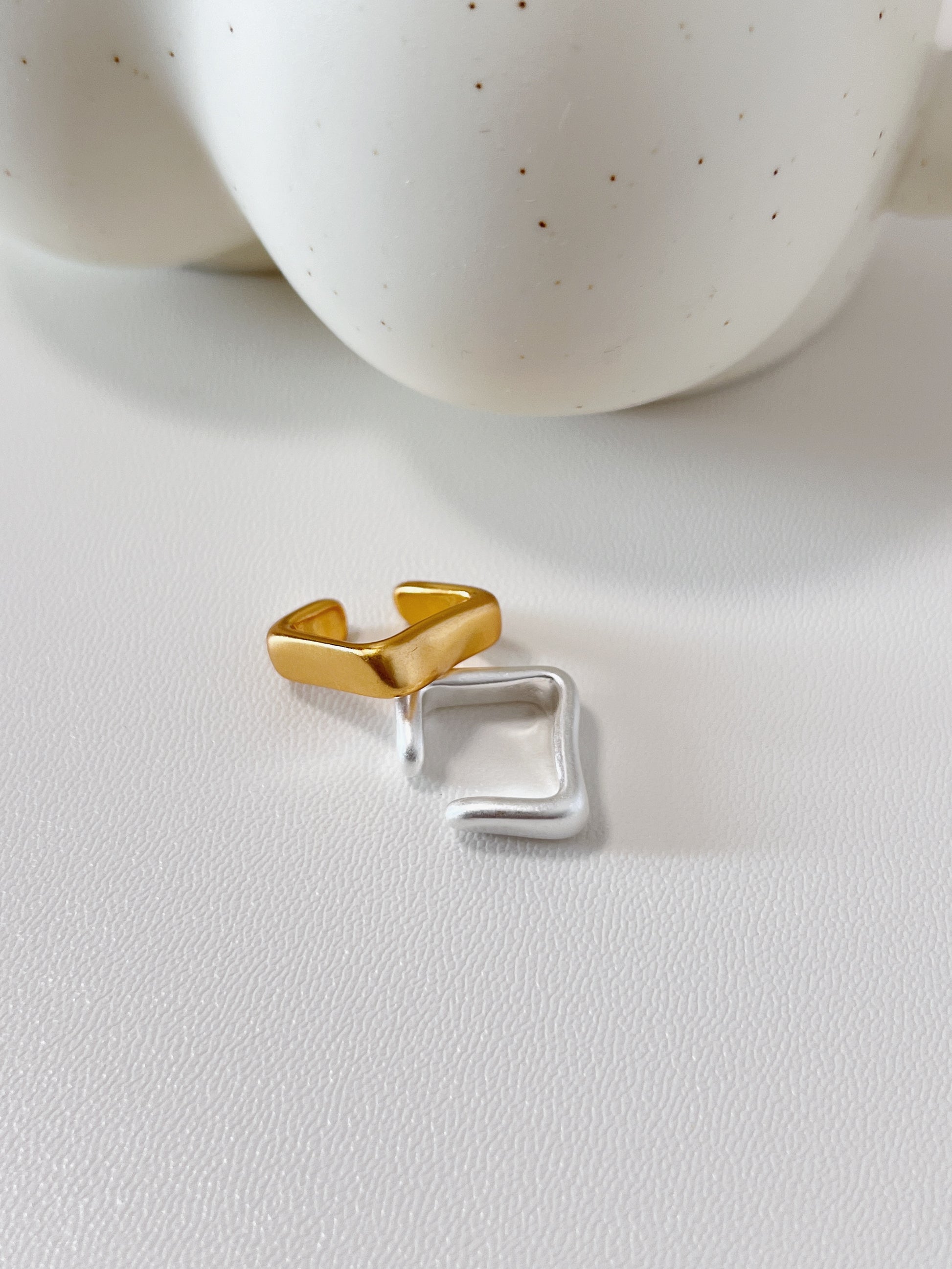Gold and silver ear cuff on a white surface with a blurred ceramic bowl in the background