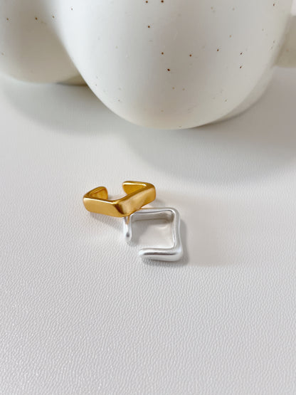 Gold and silver ear cuff on a white surface with a blurred ceramic bowl in the background