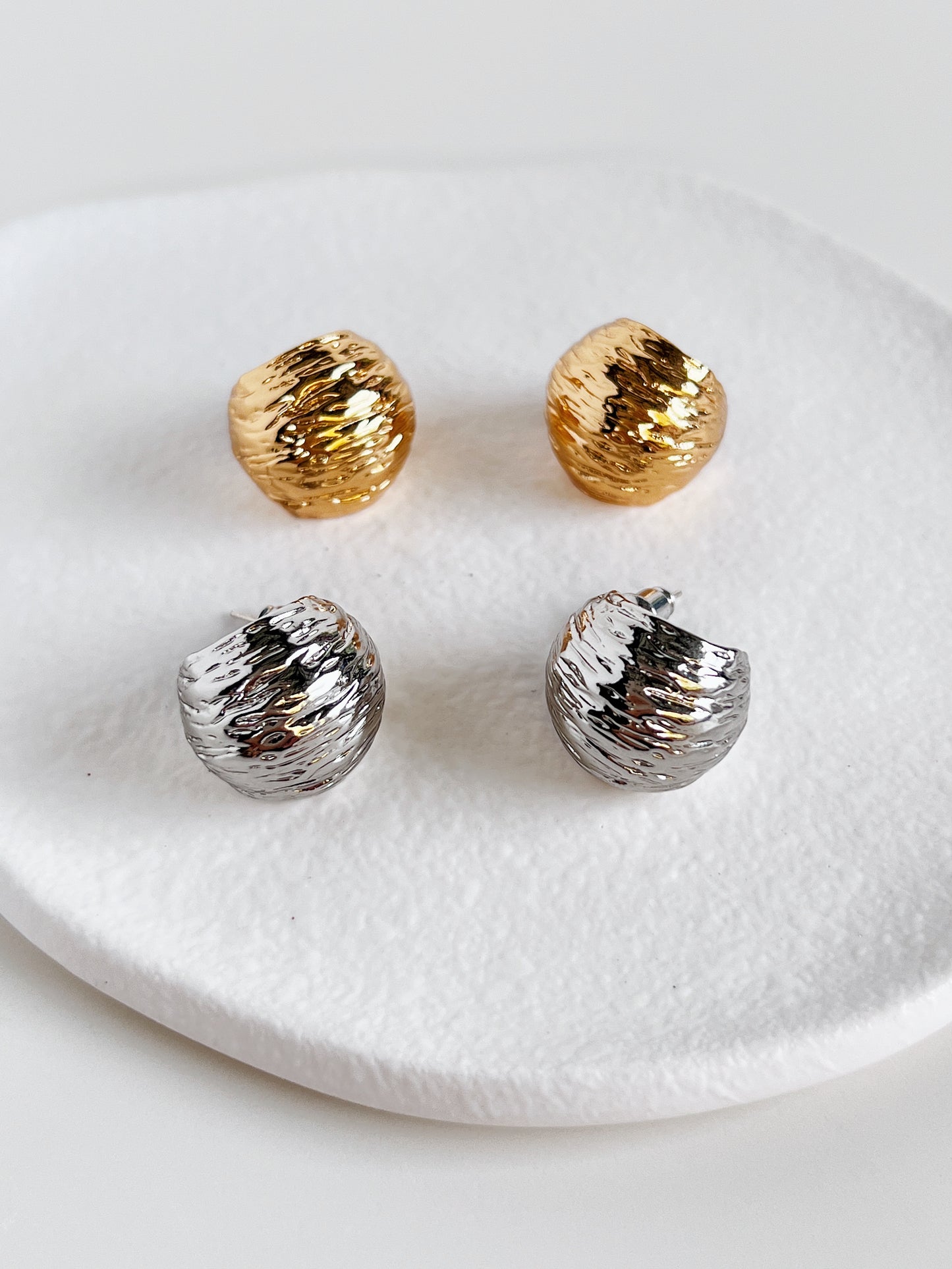 Pair of gold and silver earrings on a textured white plate