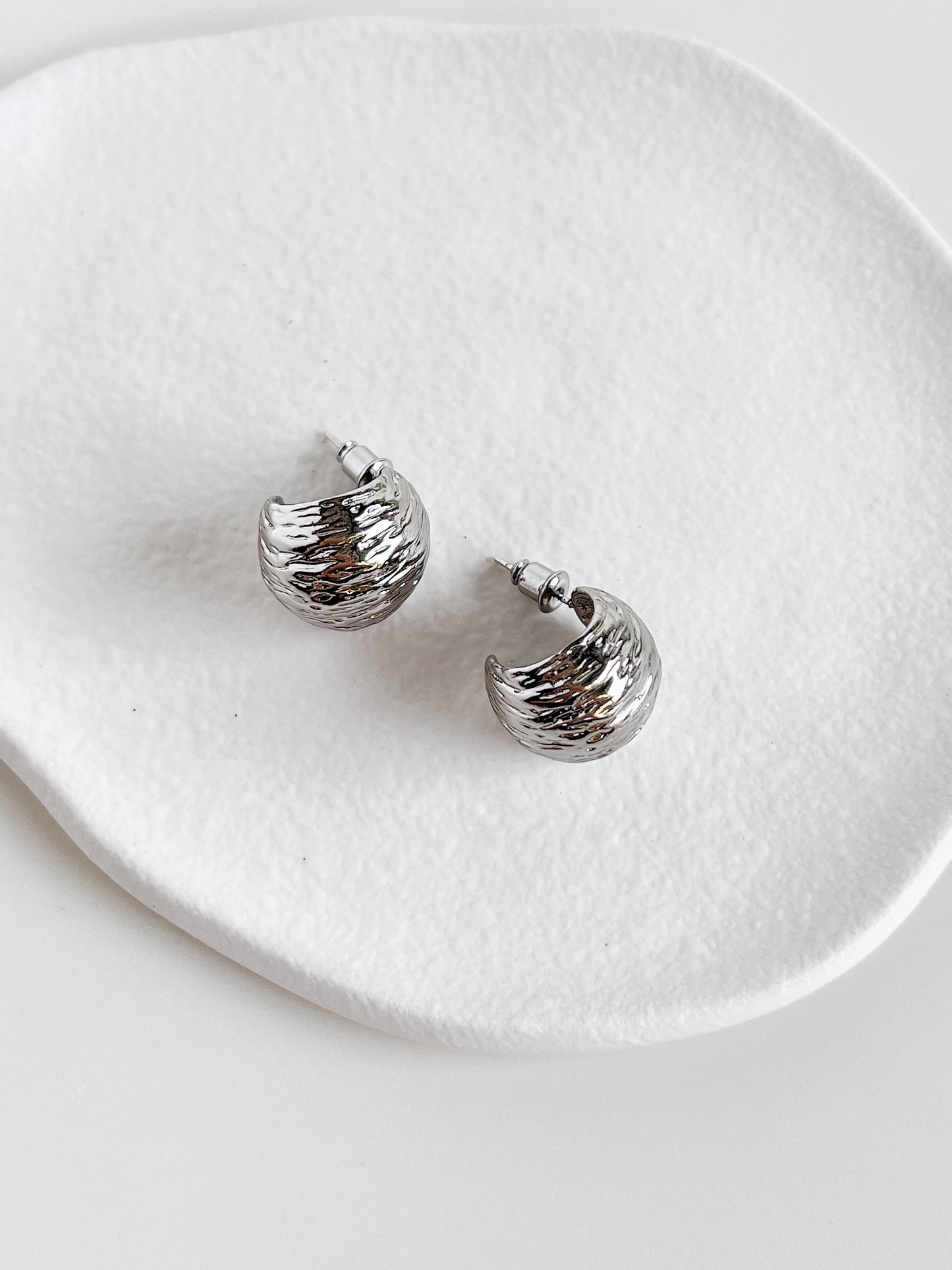 Silver hoop earrings on a white ceramic dish
