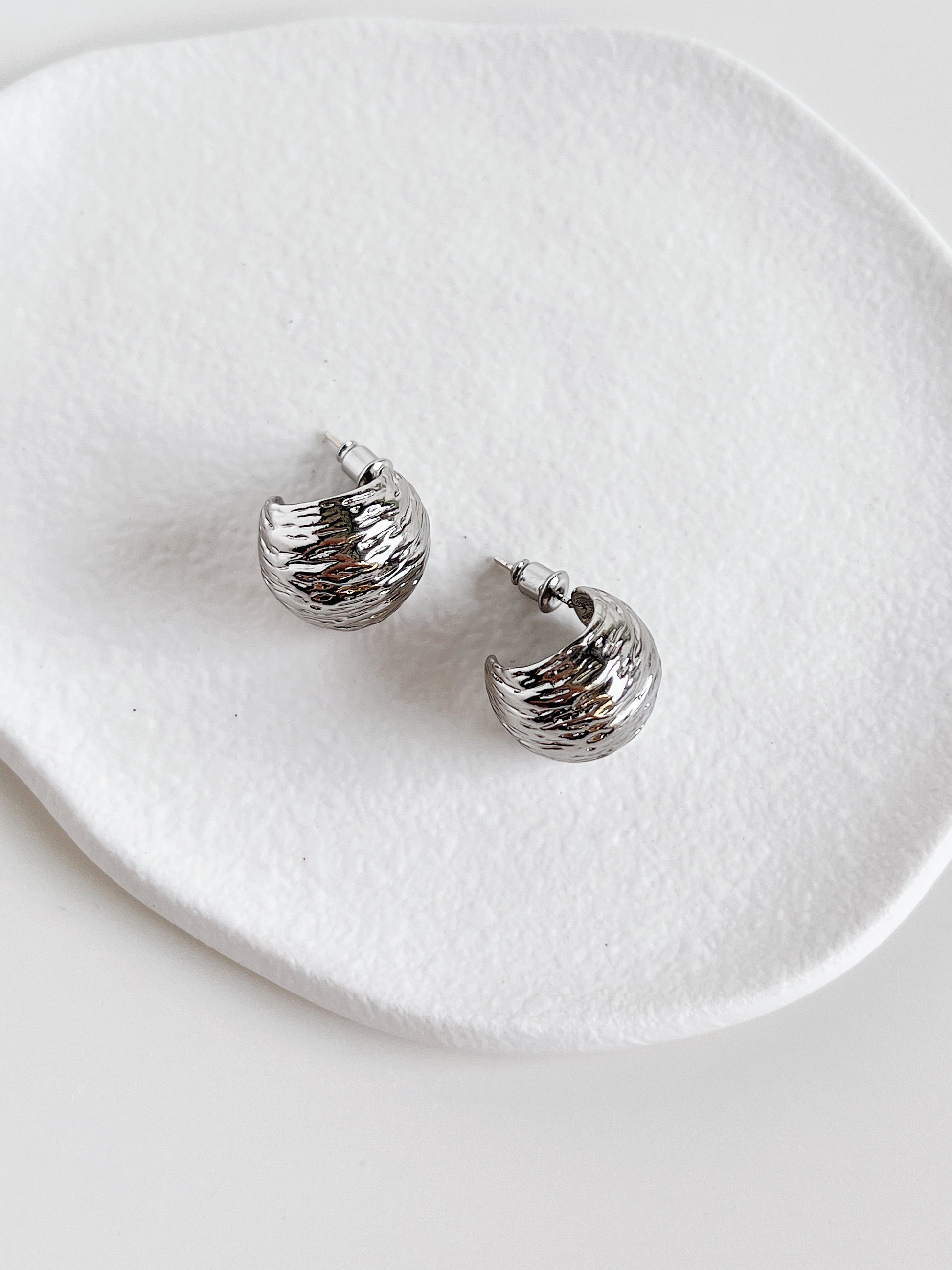 Silver hoop earrings on a white ceramic dish