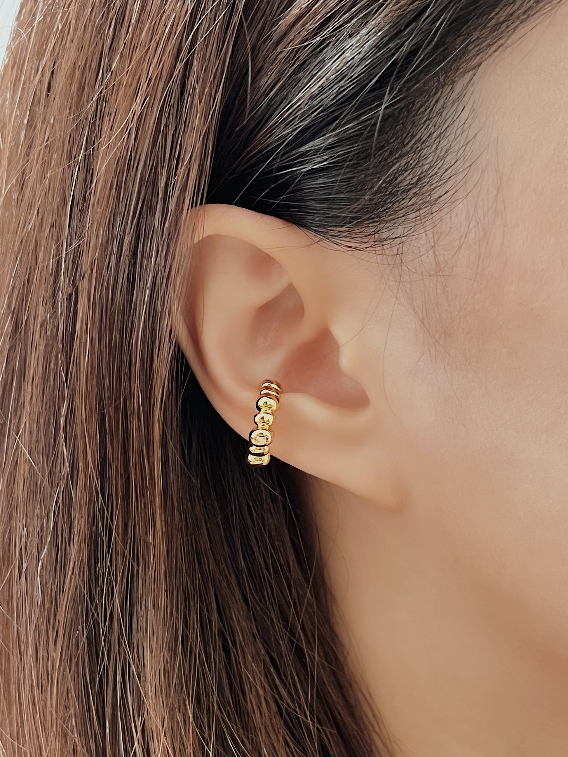 Close-up of an ear wearing a gold beaded cuff earring with hair partially obscuring the view.