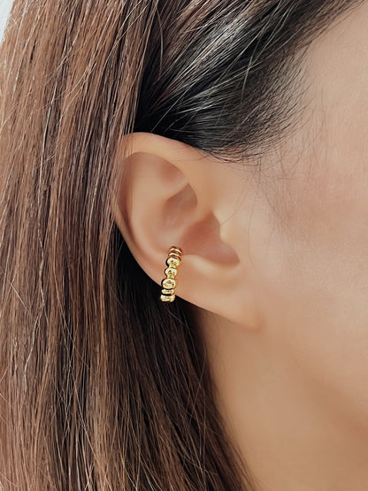 Close-up of an ear wearing a gold beaded cuff earring with hair partially obscuring the view.
