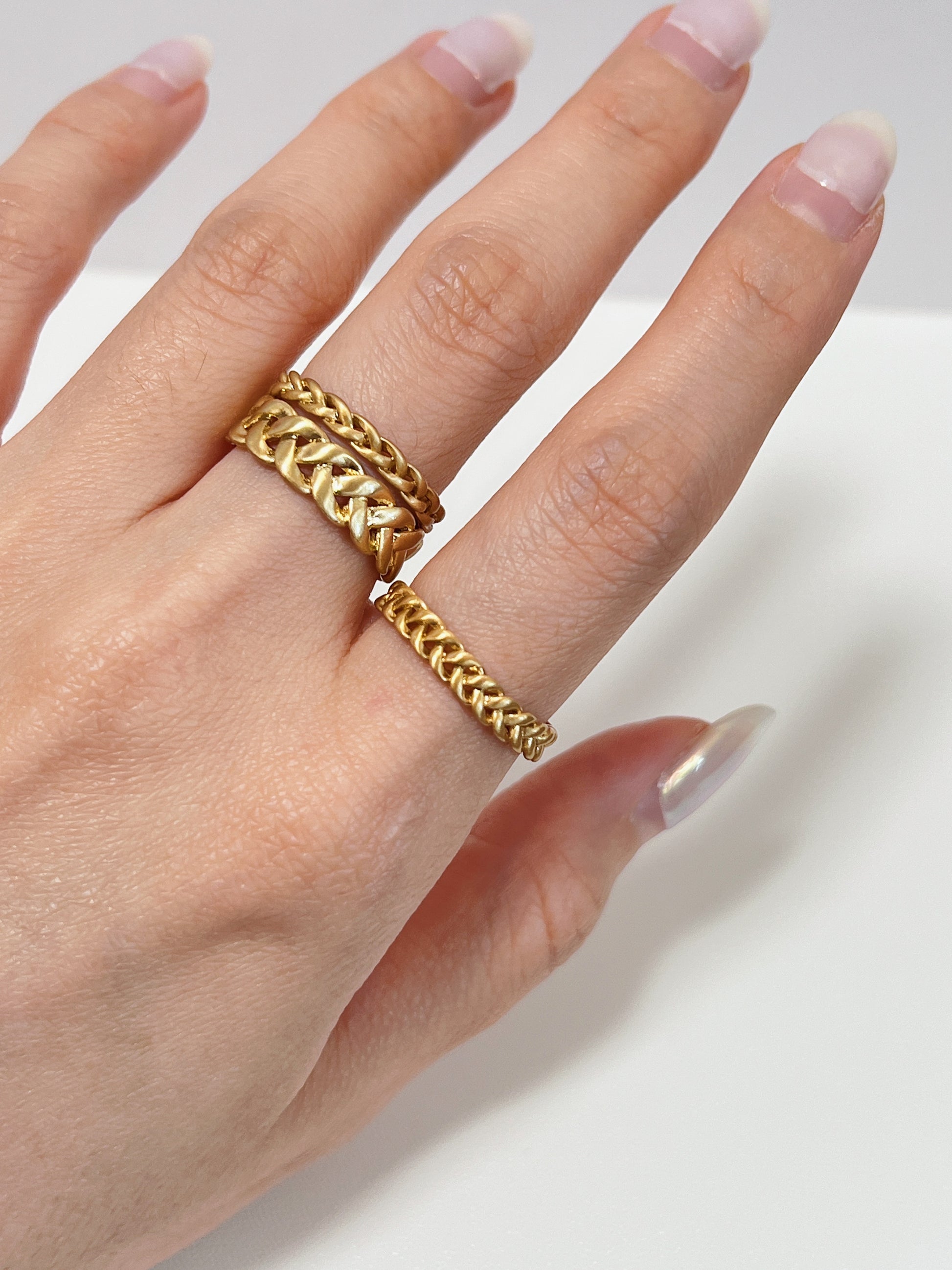 Gold braided rings on a finger against a neutral background