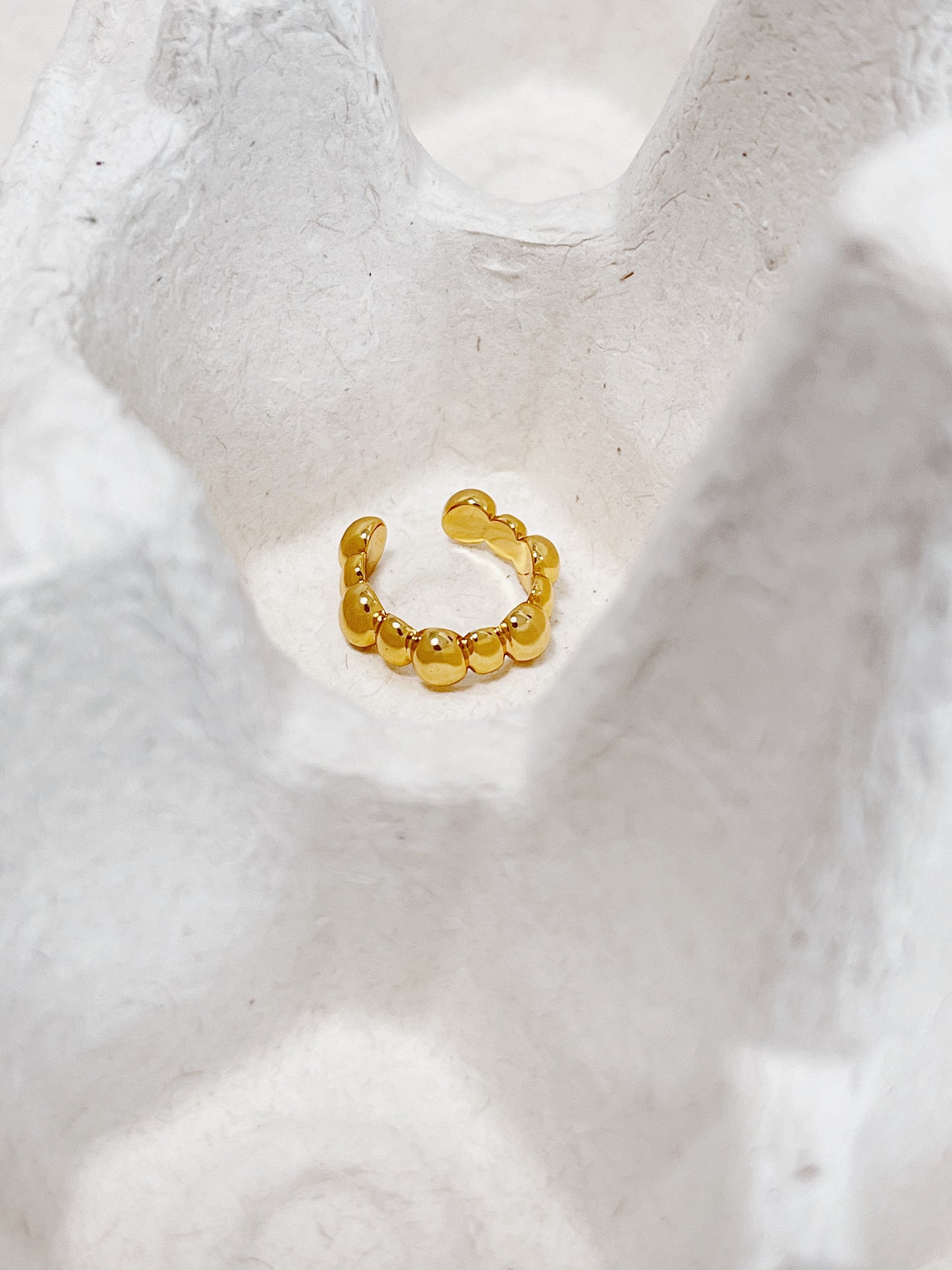 Gold beaded ear cuff earring on a textured white surface
