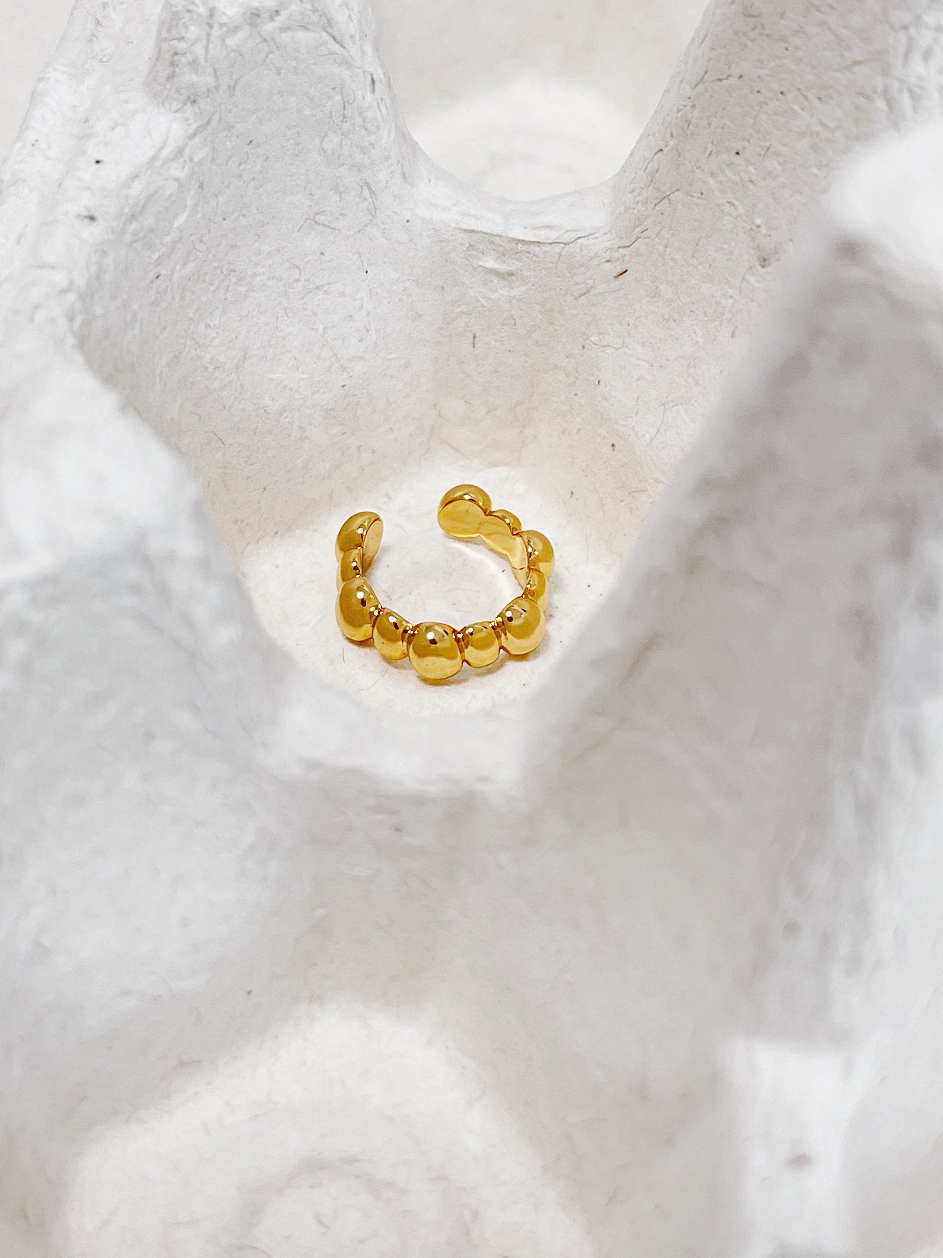 Gold beaded ear cuff earring on a textured white surface