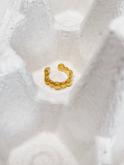 Gold beaded ear cuff earring on a textured white surface