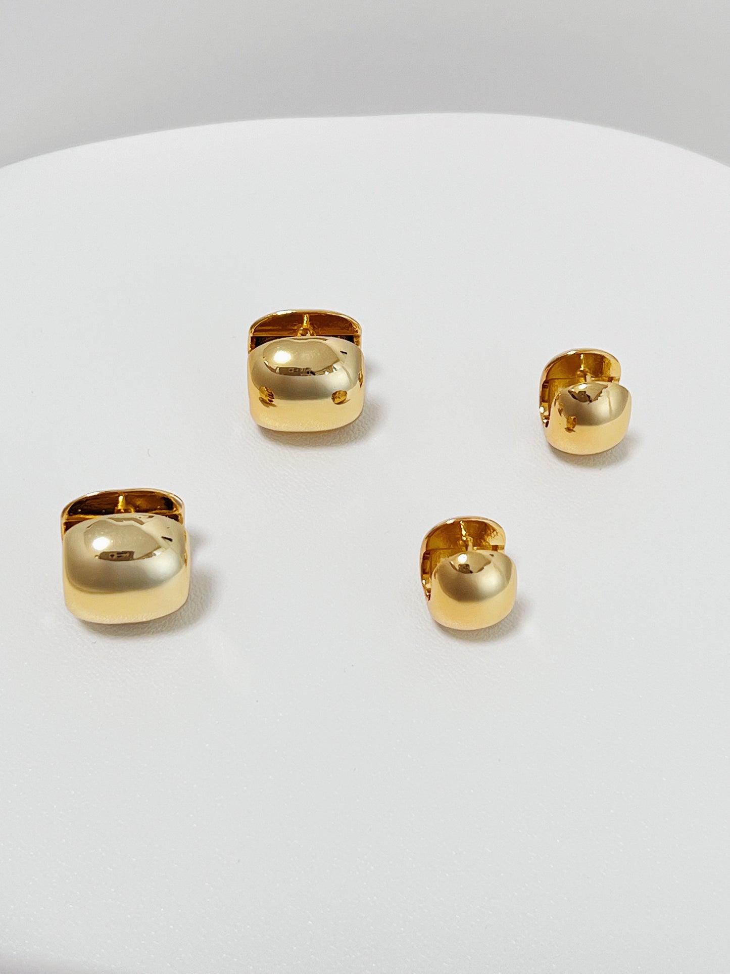 Set of 2 different sizes gold huggie hoop earrings on a white surface