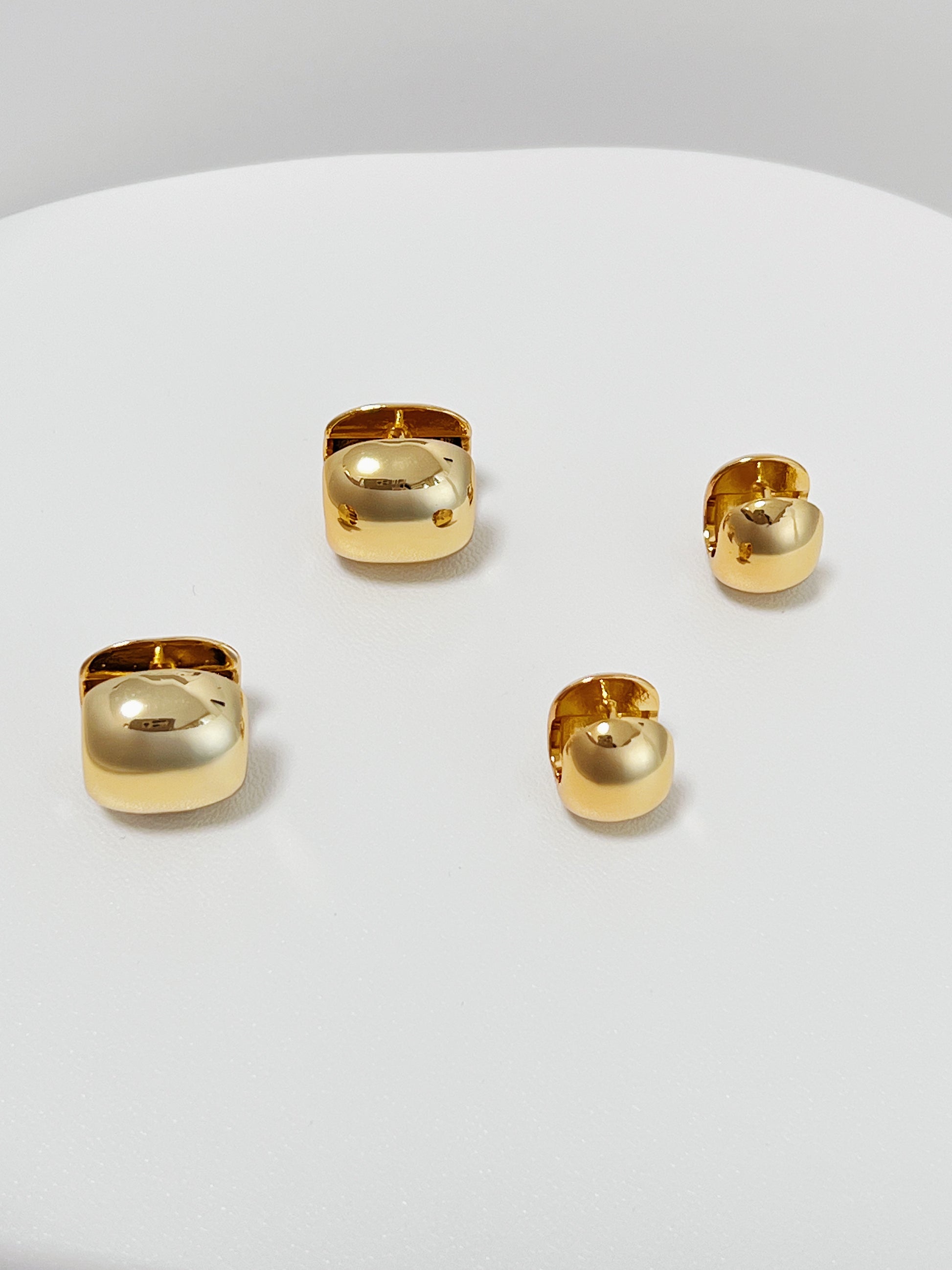 Set of 2 different sizes gold huggie hoop earrings on a white surface