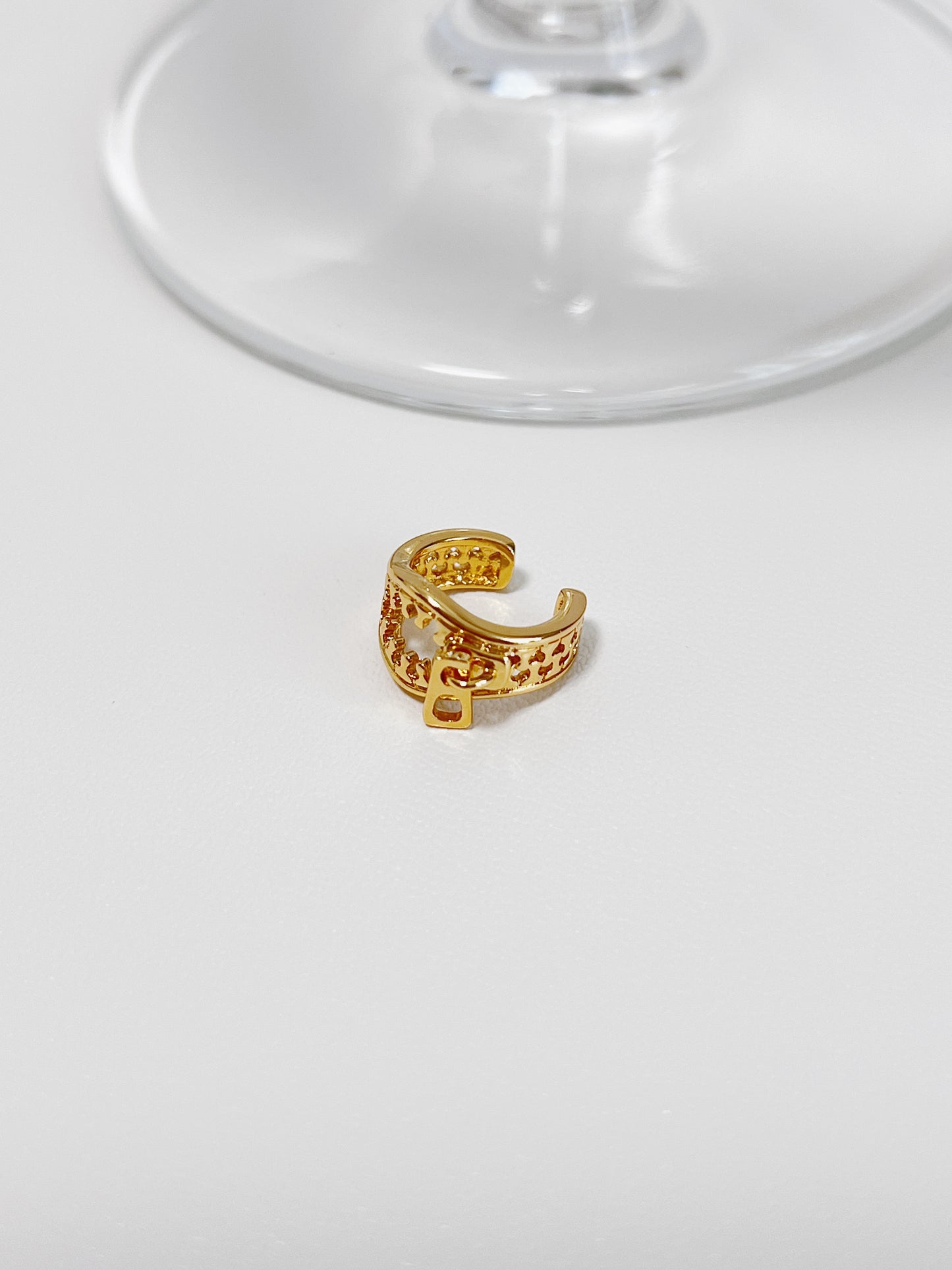 Gold zipper ear cuff on a white surface with a clear glass object in the background