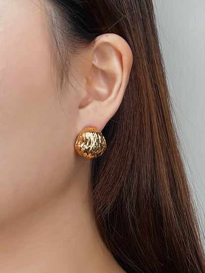 Close-up of a person wearing gold hoop earrings with a neutral background