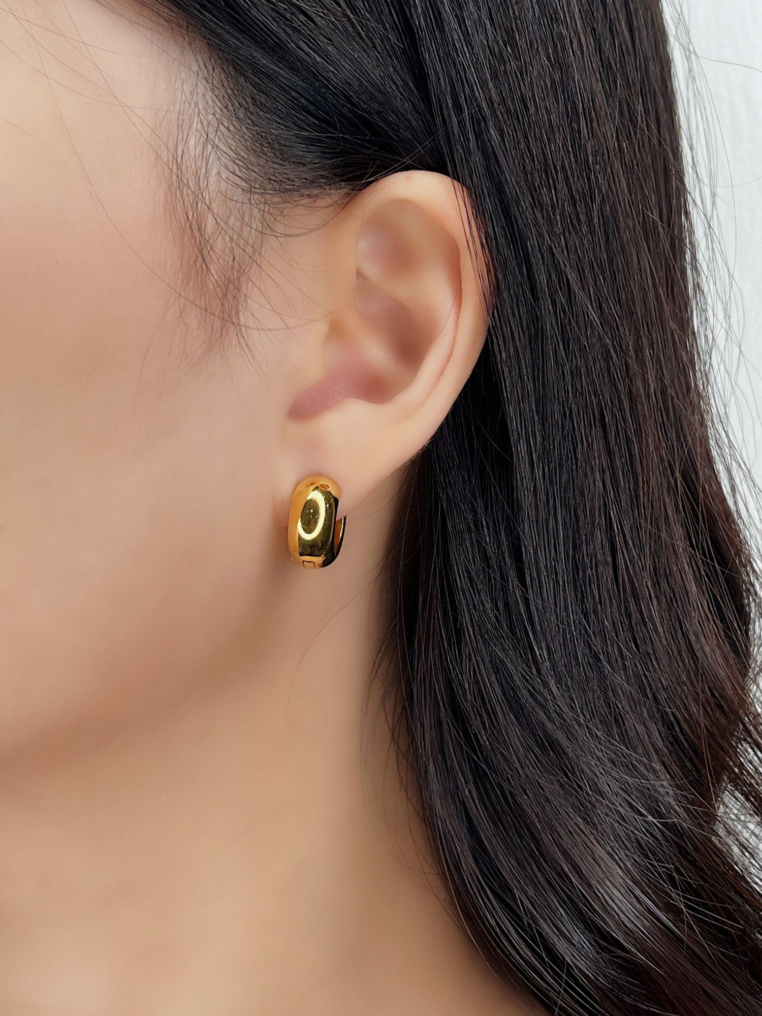 Gold hoop earrings worn by a person with dark hair.