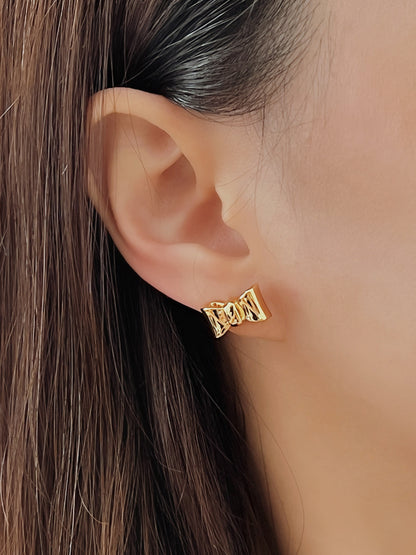 Gold bow stud earring worn by a person with brown hair.