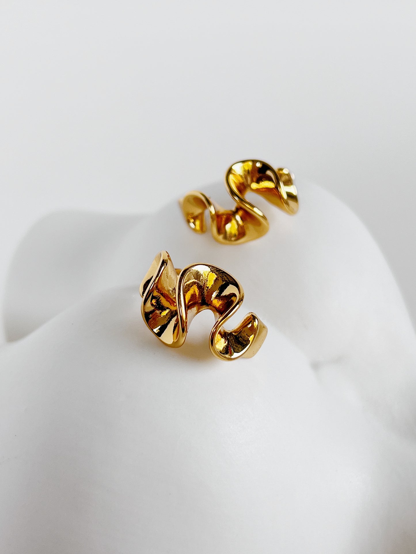 Pair of gold spiral wavy earrings on a white ceramic background