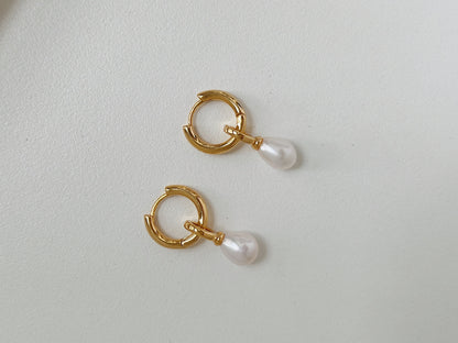 A pair of gold dangle pearl earrings flatlay on a white background.