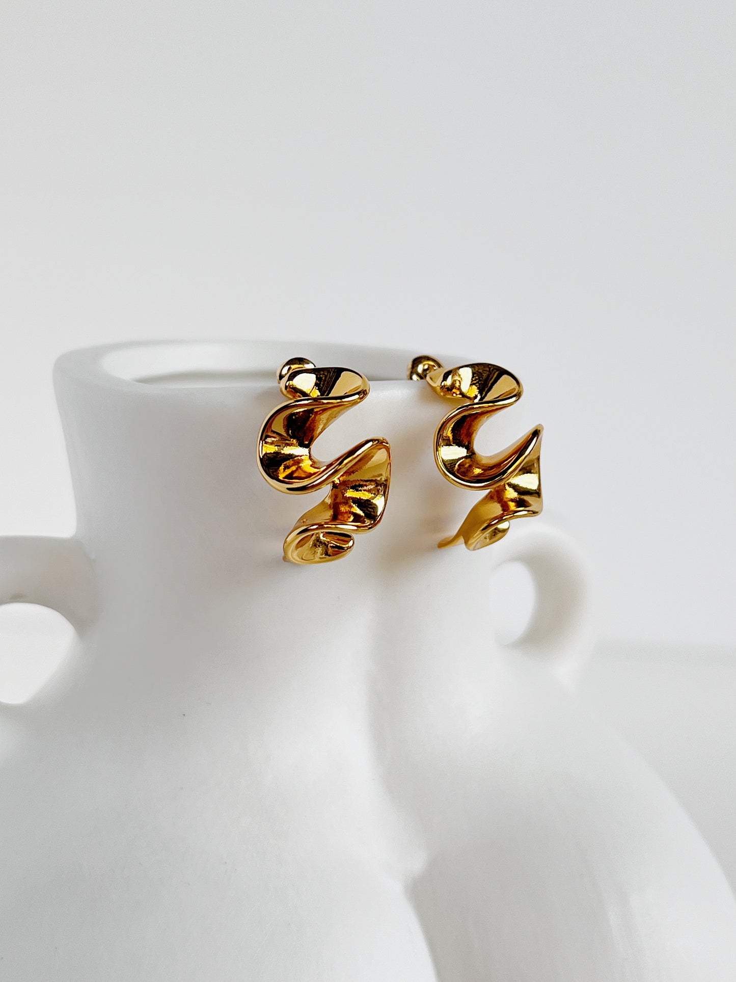 Gold spiral earrings on a white ceramic bust stand