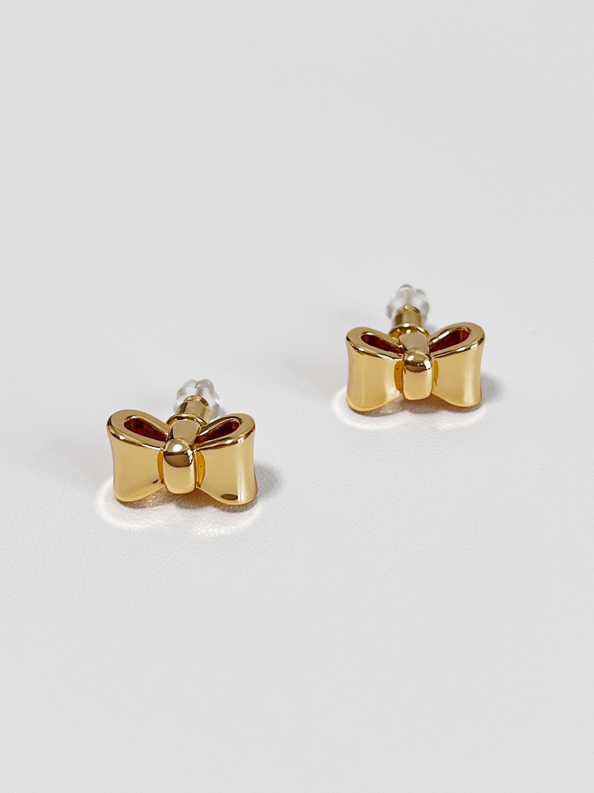 Gold bow-shaped earrings on a light gray background
