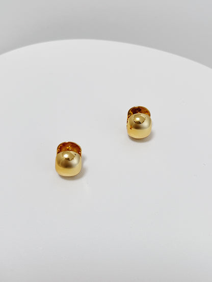 Pair of gold huggie earrings on a white surface with a gray background