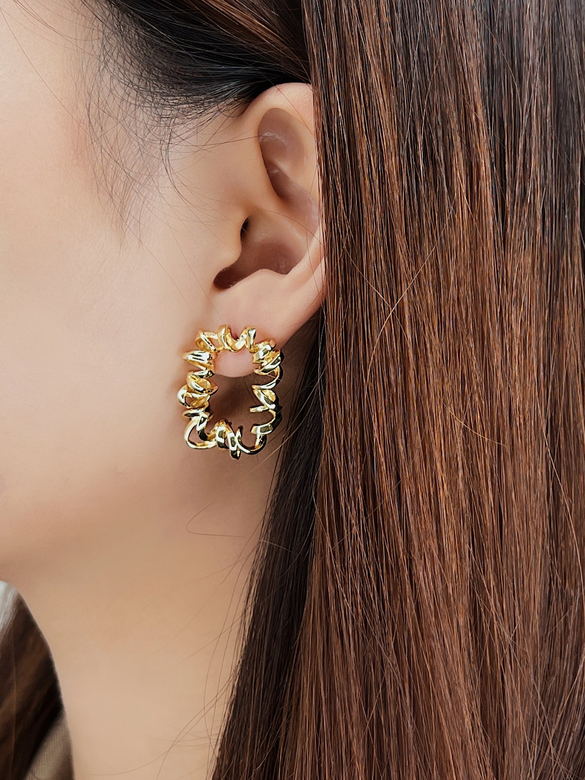 Close-up of a person wearing gold spiral hoop earrings with a neutral background