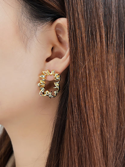 Close-up of a person wearing gold spiral hoop earrings with a neutral background