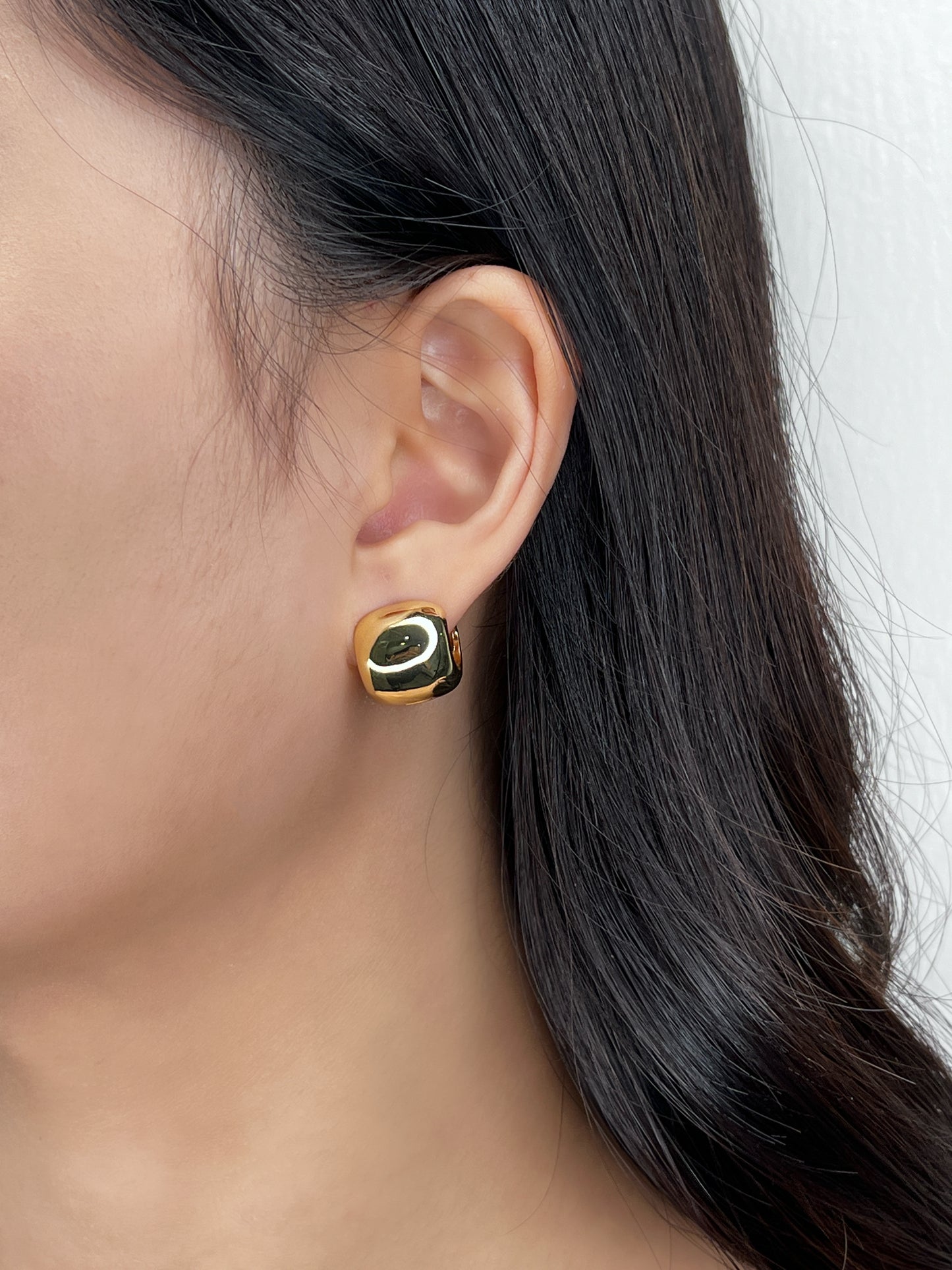 Gold wide huggie earring worn by a person with dark hair.
