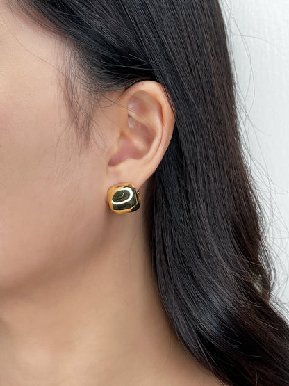 Gold wide huggie earring worn by a person with dark hair.
