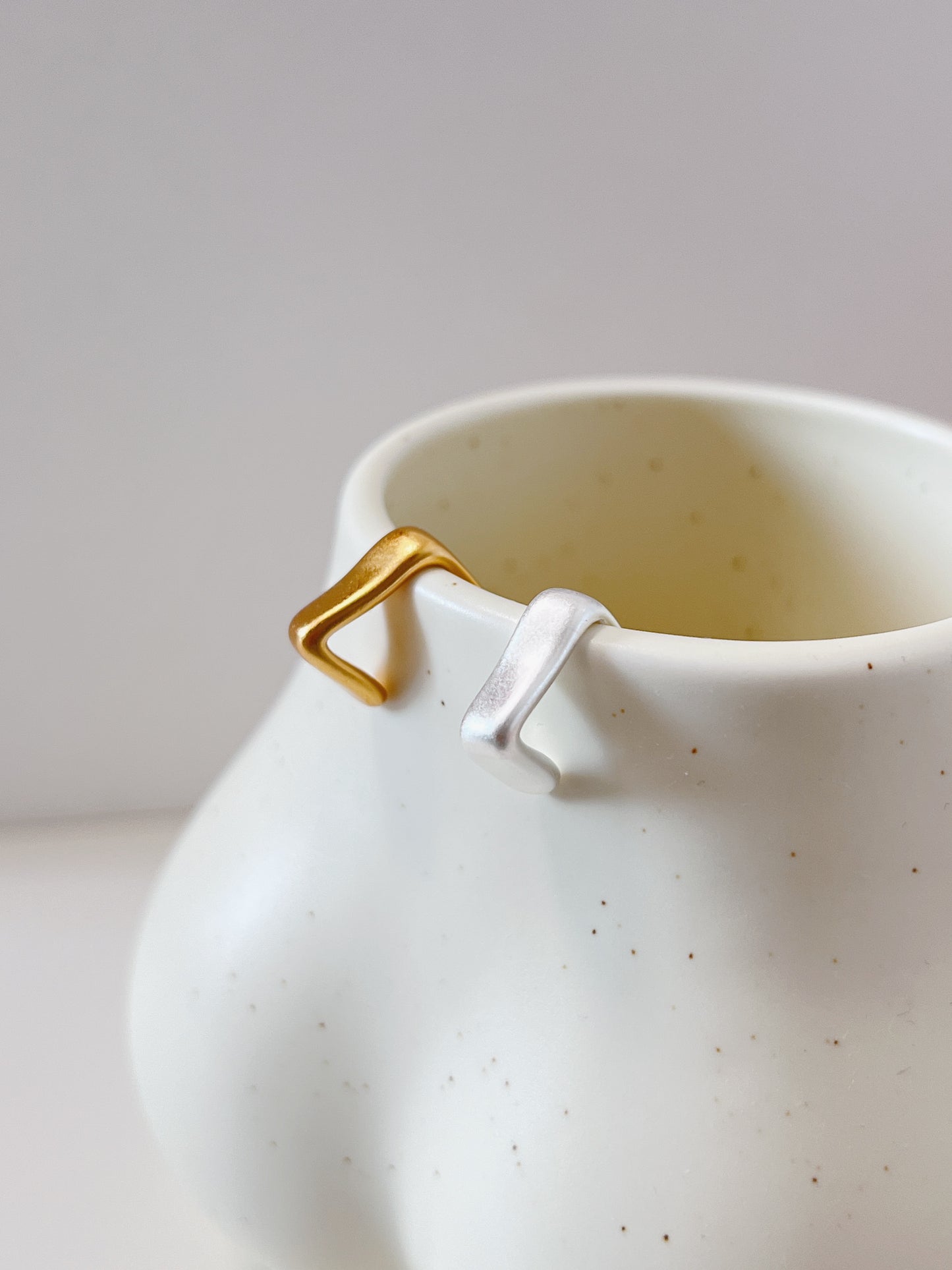 White ceramic mug with gold and silver geometric cuff earrings on a light gray background