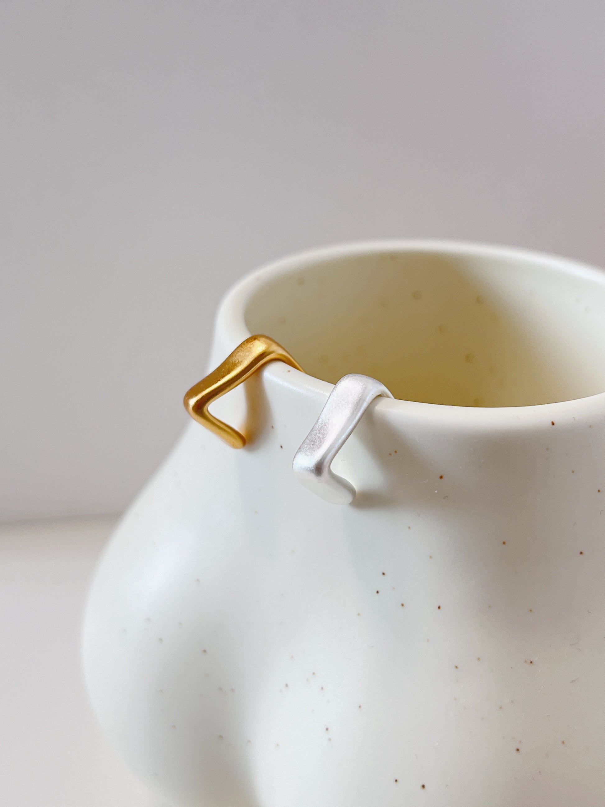 White ceramic mug with gold and silver geometric cuff earrings on a light gray background