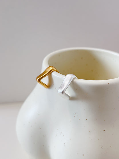 White ceramic mug with gold and silver geometric cuff earrings on a light gray background
