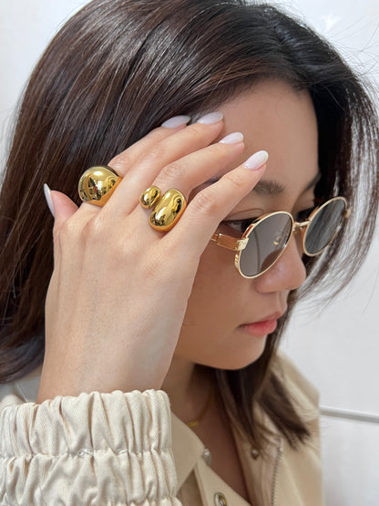 Woman wearing gold sunglasses and rings on a plain background