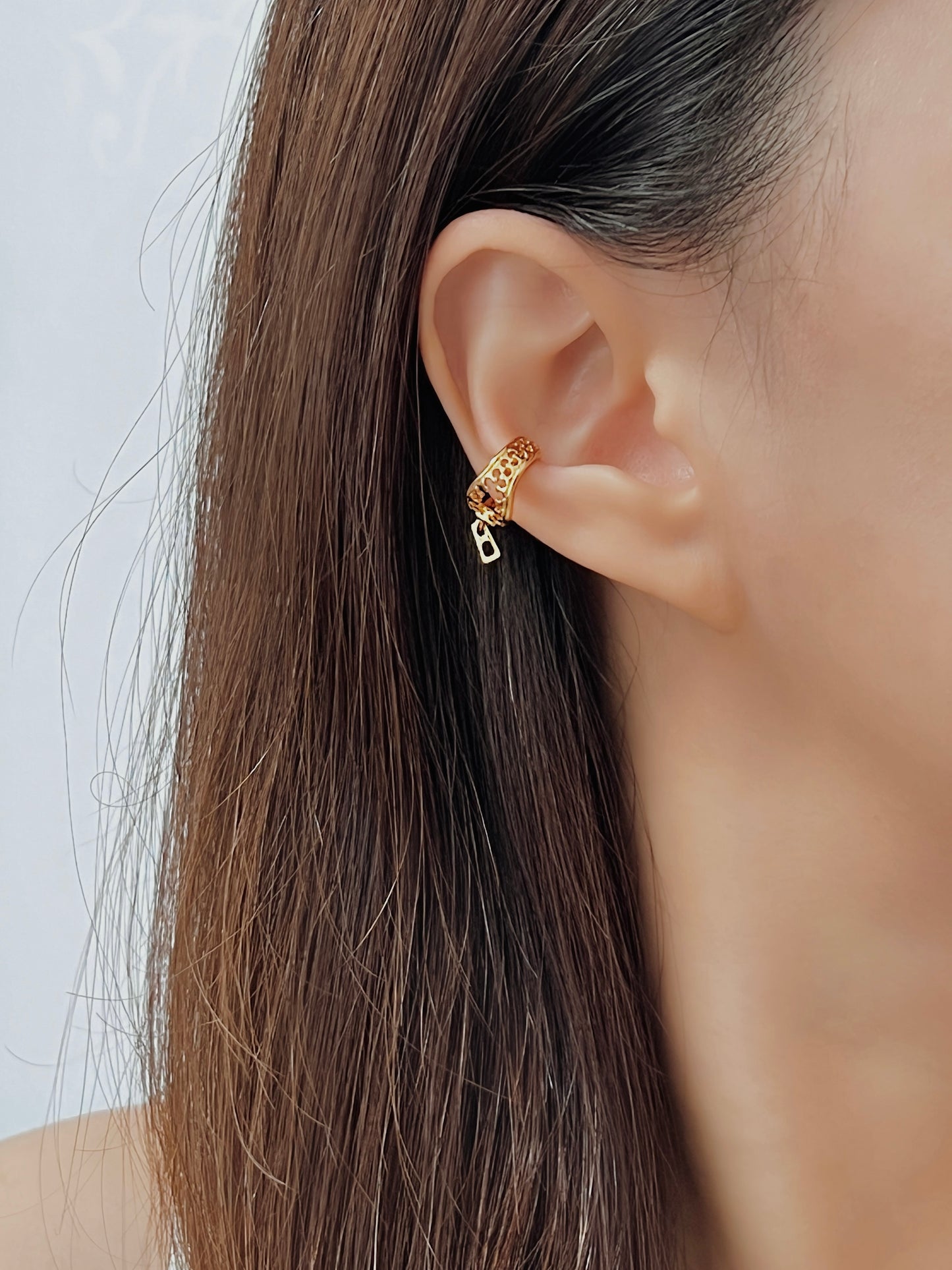 Close-up of a person wearing a gold zipper ear cuff with a plain background