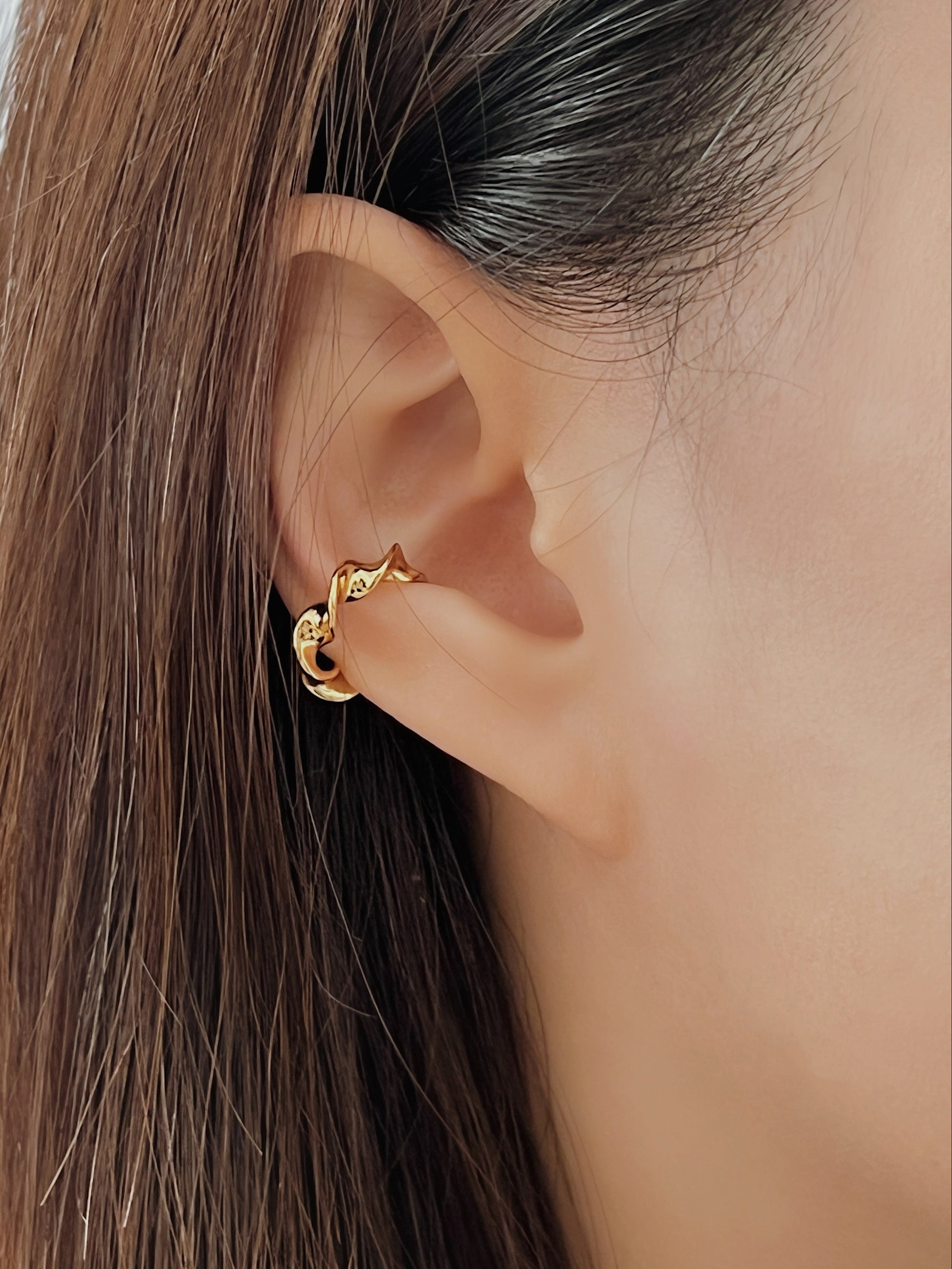 Close-up of a person wearing a gold twist ear cuff