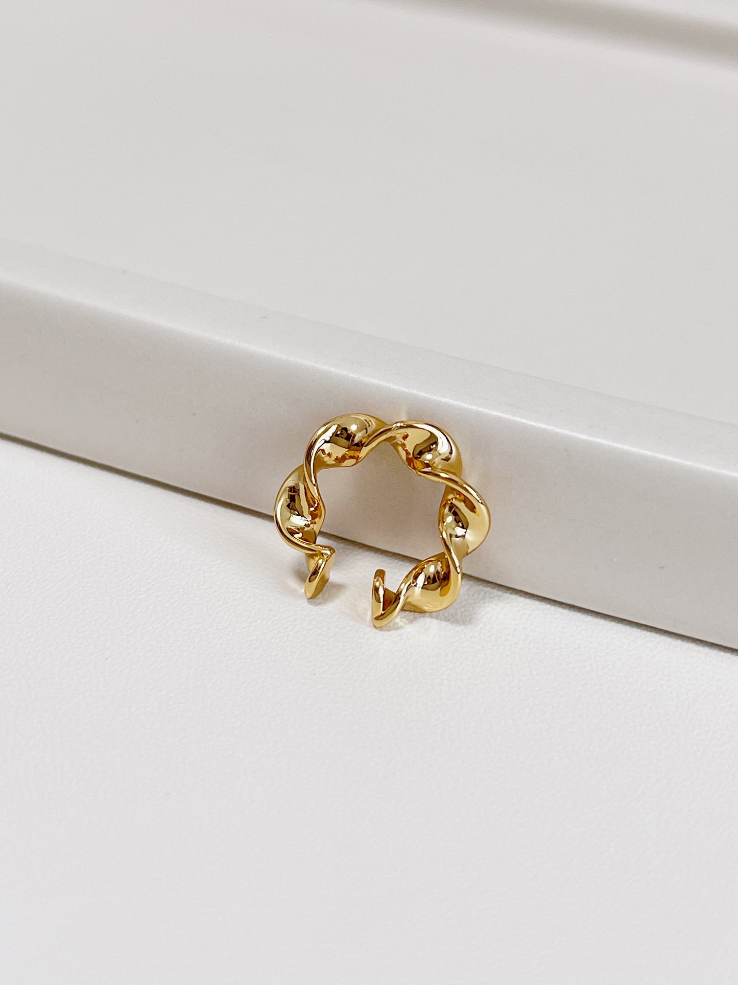 Gold twisted ear cuff on a white surface